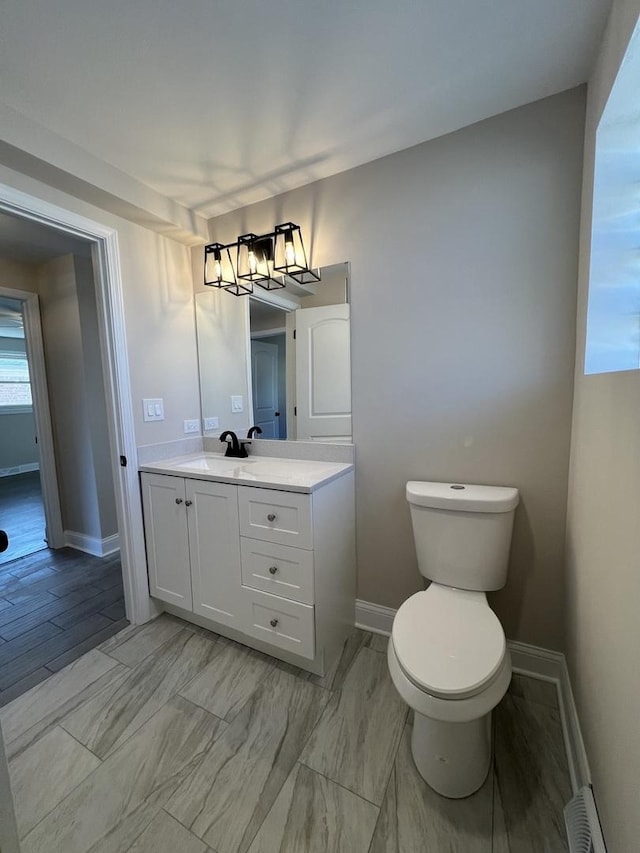 bathroom featuring baseboard heating, toilet, vanity, and baseboards