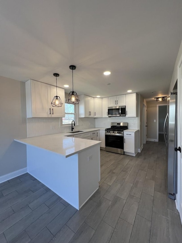 kitchen with backsplash, a peninsula, white cabinets, stainless steel appliances, and a sink