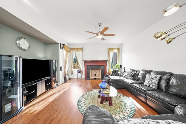 living area featuring a fireplace, ceiling fan, and wood finished floors