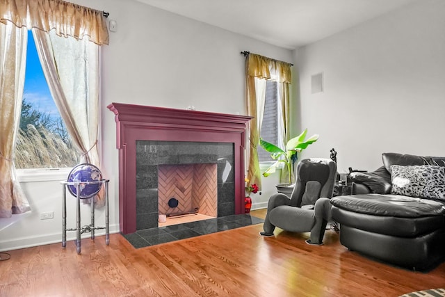 living area featuring a tiled fireplace, plenty of natural light, wood finished floors, and baseboards