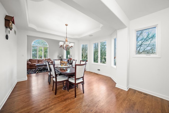 dining area with a tray ceiling, baseboards, an inviting chandelier, and wood finished floors