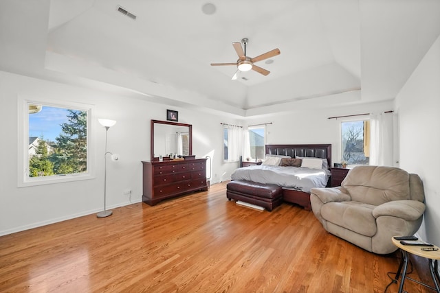 bedroom with light wood finished floors, multiple windows, and a raised ceiling