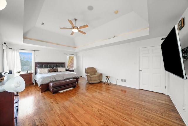 bedroom featuring a raised ceiling, light wood-style floors, visible vents, and ceiling fan