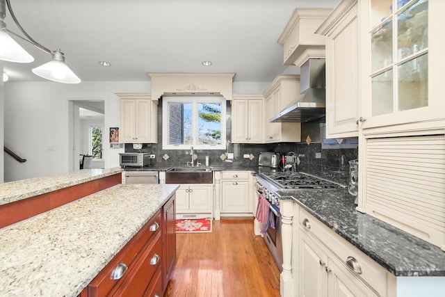 kitchen featuring light wood-type flooring, a sink, stainless steel range, wall chimney exhaust hood, and tasteful backsplash