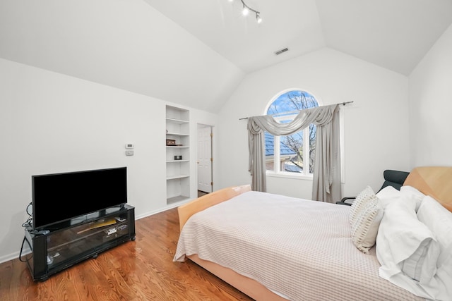 bedroom with visible vents, baseboards, wood finished floors, and vaulted ceiling