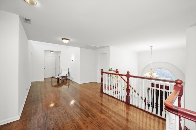 hallway with visible vents, an upstairs landing, wood finished floors, an inviting chandelier, and baseboards