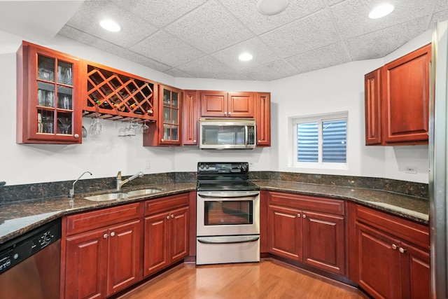 kitchen featuring light wood finished floors, dark stone counters, a sink, stainless steel appliances, and glass insert cabinets