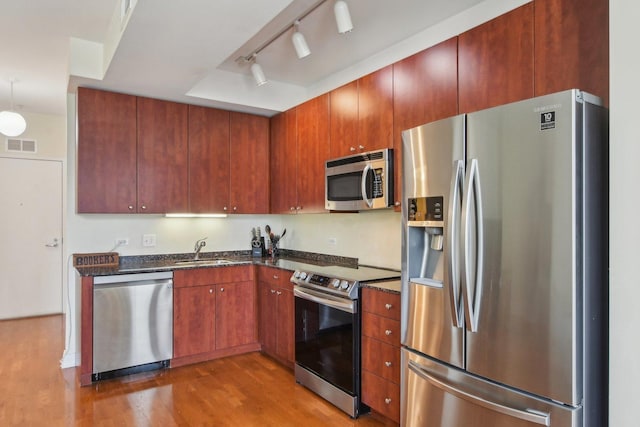 kitchen featuring visible vents, dark stone countertops, appliances with stainless steel finishes, wood finished floors, and a sink