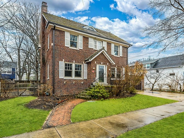 view of front of home featuring brick siding, a chimney, a front yard, and fence