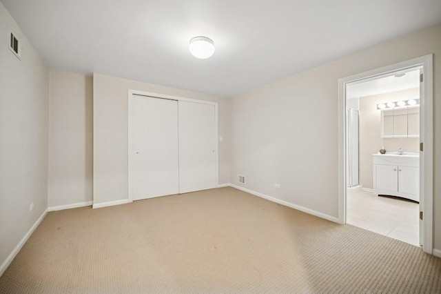 unfurnished bedroom featuring a sink, a closet, baseboards, and light colored carpet