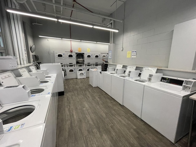 community laundry room with stacked washing maching and dryer, concrete block wall, dark wood-style flooring, and washer and clothes dryer