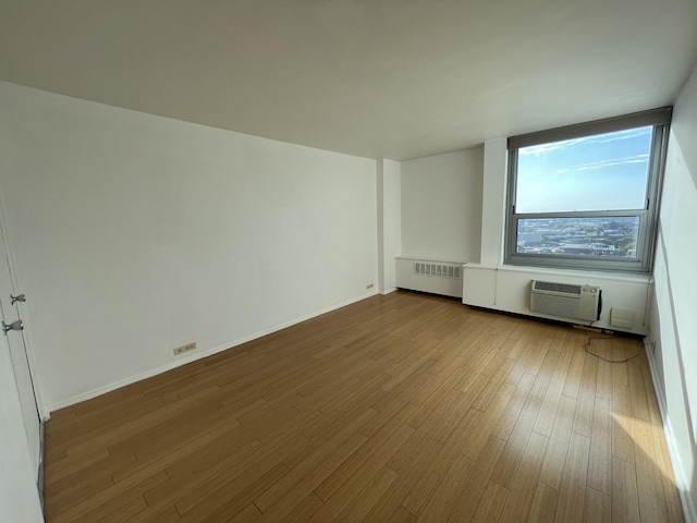 empty room with baseboards, radiator, wood finished floors, and a wall mounted AC