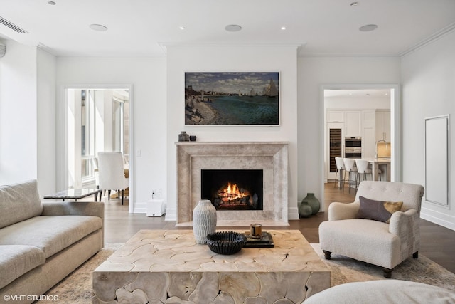 living room with a high end fireplace, visible vents, wood finished floors, and ornamental molding