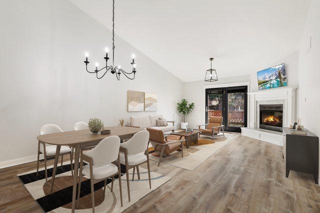 dining room featuring high vaulted ceiling, baseboards, light wood finished floors, and a lit fireplace