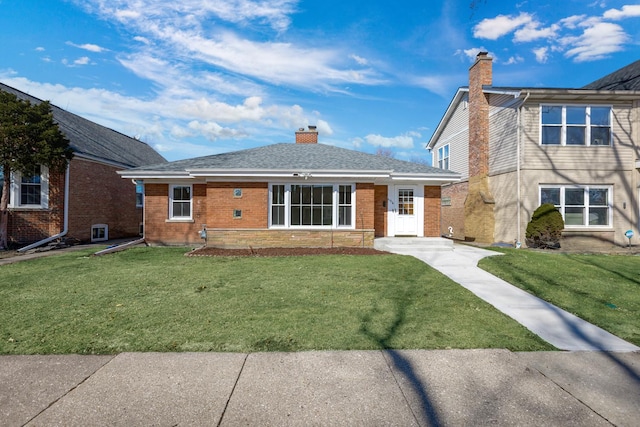 view of front of property featuring brick siding, a chimney, a front lawn, and roof with shingles