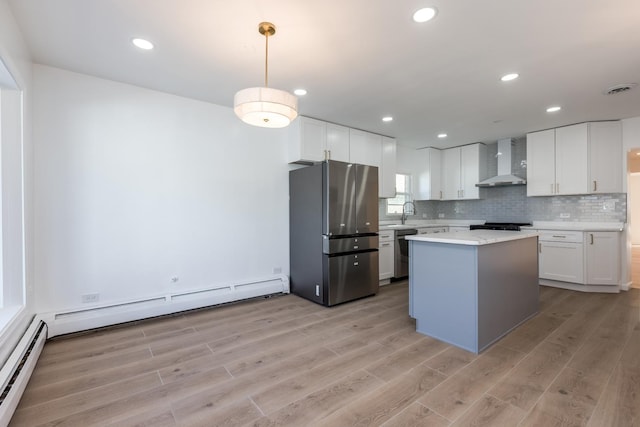 kitchen featuring a baseboard radiator, appliances with stainless steel finishes, light countertops, and wall chimney range hood