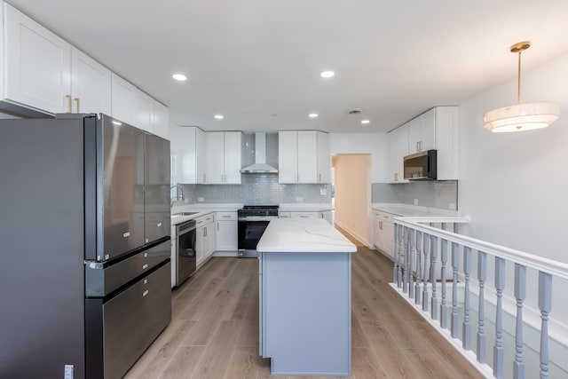 kitchen with light wood finished floors, wall chimney exhaust hood, appliances with stainless steel finishes, and a center island