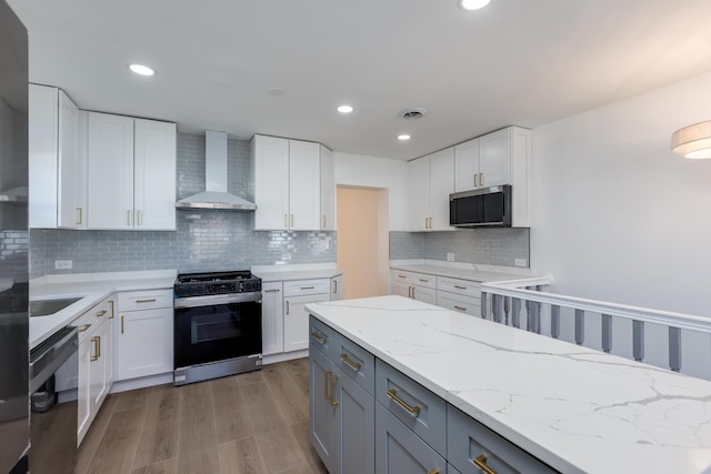 kitchen with stainless steel microwave, wall chimney range hood, dishwasher, white cabinets, and gas stove