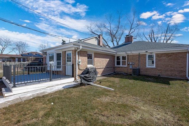 rear view of property with brick siding, a shingled roof, cooling unit, a chimney, and a yard