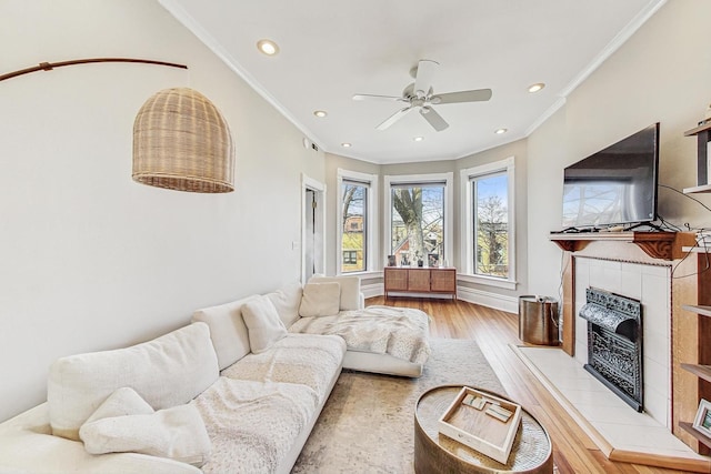 living area with light wood-style flooring, recessed lighting, ceiling fan, a tiled fireplace, and crown molding