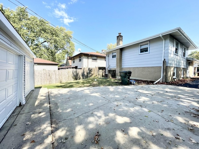 back of property with fence, a garage, brick siding, a chimney, and a patio area