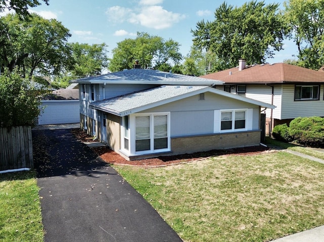 view of side of property with brick siding, fence, roof with shingles, a yard, and an outbuilding