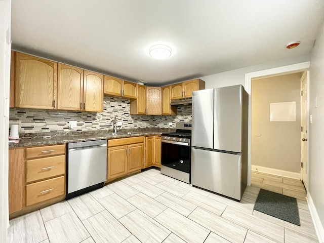 kitchen featuring a sink, stainless steel appliances, under cabinet range hood, dark countertops, and tasteful backsplash