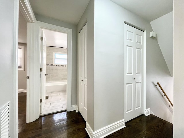 hallway with an upstairs landing, visible vents, baseboards, and dark wood-style flooring