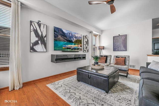 living room with ceiling fan, visible vents, baseboards, and wood finished floors