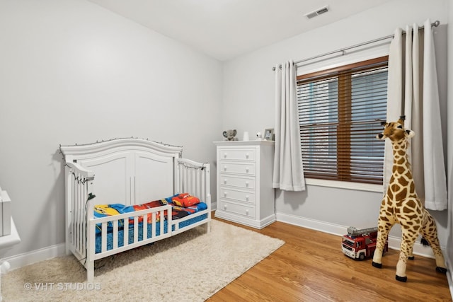 bedroom with visible vents, a nursery area, baseboards, and light wood-style floors