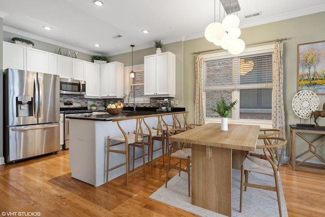 kitchen with visible vents, stainless steel appliances, white cabinets, crown molding, and dark countertops