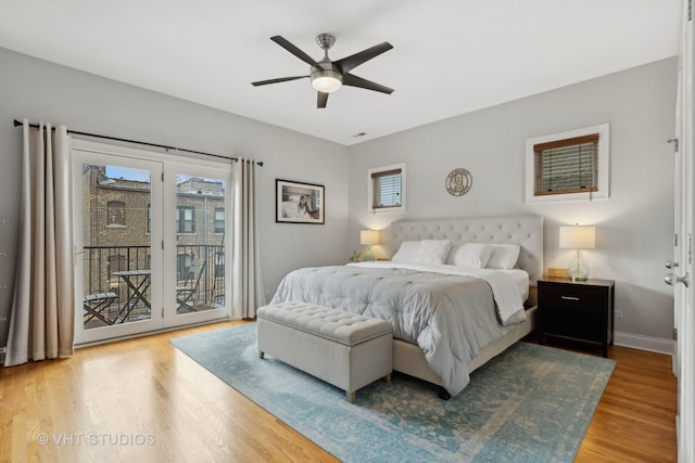 bedroom featuring access to exterior, multiple windows, baseboards, and wood finished floors