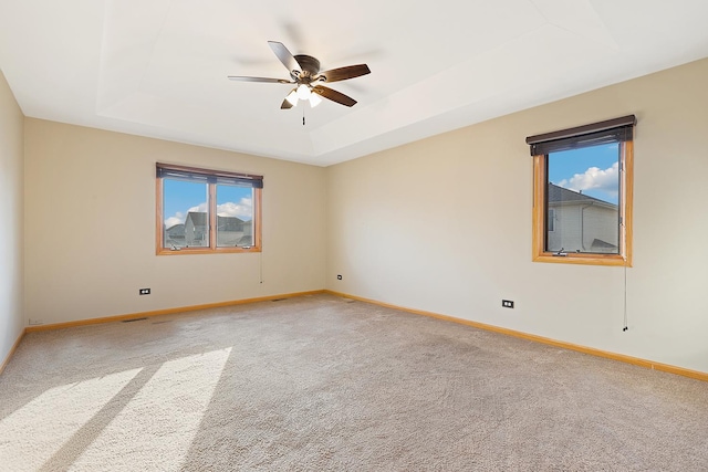 empty room featuring light carpet, baseboards, a raised ceiling, and ceiling fan