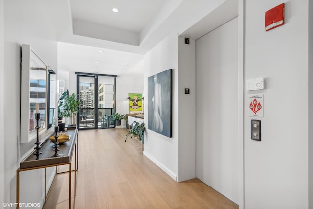 hallway featuring elevator, recessed lighting, baseboards, and light wood-style floors