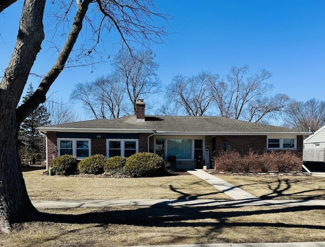 ranch-style house with brick siding, a chimney, and roof with shingles