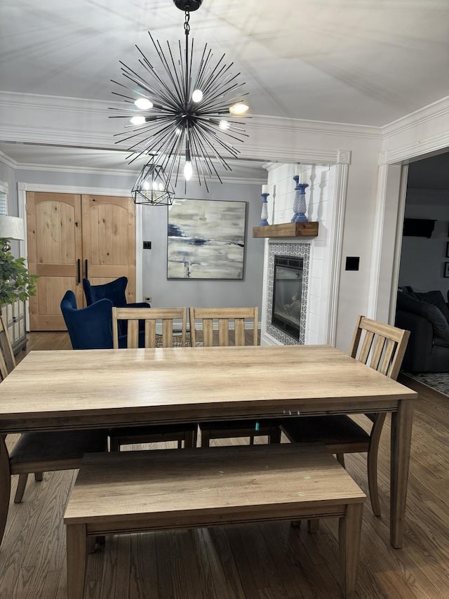 dining space with an inviting chandelier, ornamental molding, wood finished floors, and a tile fireplace