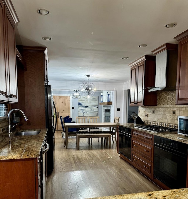 kitchen featuring black appliances, a sink, wall chimney range hood, light wood finished floors, and decorative backsplash