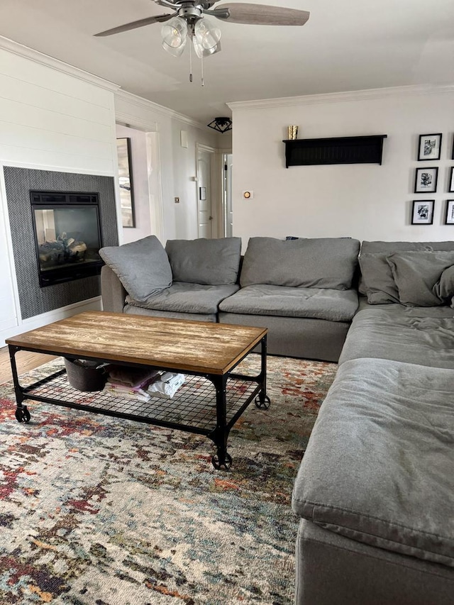 living room featuring a ceiling fan, a glass covered fireplace, and crown molding