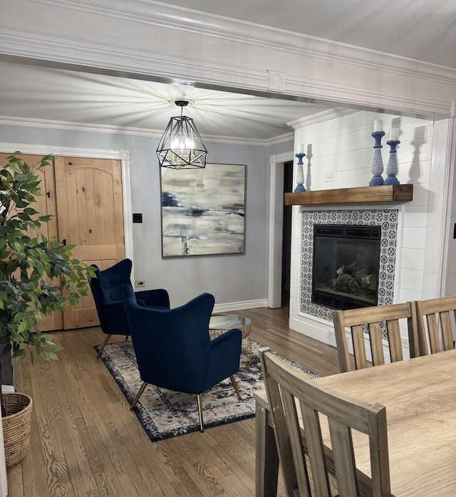 living room with a tiled fireplace, crown molding, wood finished floors, and an inviting chandelier