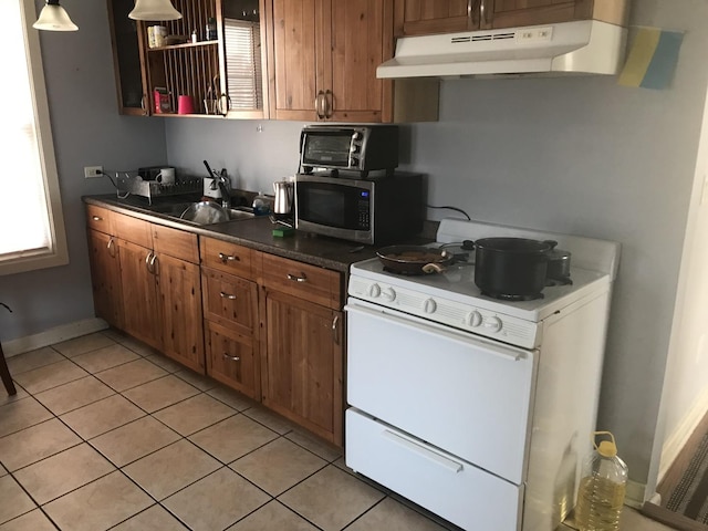 kitchen with dark countertops, brown cabinetry, white gas stove, under cabinet range hood, and stainless steel microwave