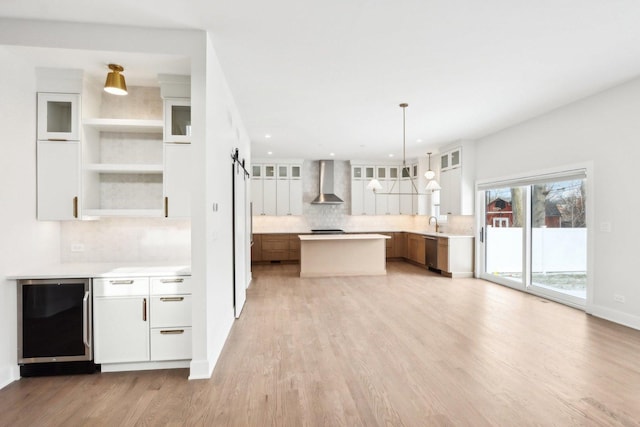 kitchen featuring light wood-style flooring, wine cooler, stainless steel dishwasher, a barn door, and wall chimney exhaust hood