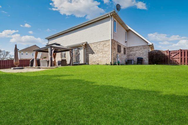 rear view of property with central air condition unit, a lawn, stone siding, a fenced backyard, and a gazebo