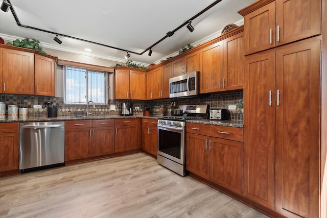 kitchen featuring dark stone counters, decorative backsplash, brown cabinetry, stainless steel appliances, and a sink