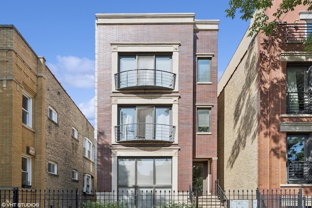 view of front of property with brick siding, a balcony, and fence