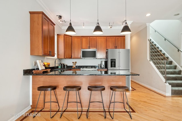 kitchen with dark stone counters, ornamental molding, a peninsula, brown cabinetry, and stainless steel appliances