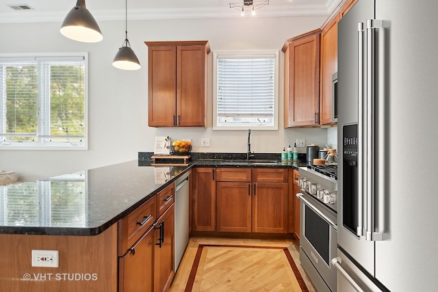 kitchen with brown cabinetry, a peninsula, a sink, crown molding, and high quality appliances