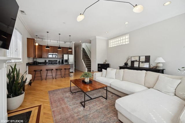 living area featuring stairway, visible vents, light wood-style floors, and ornamental molding