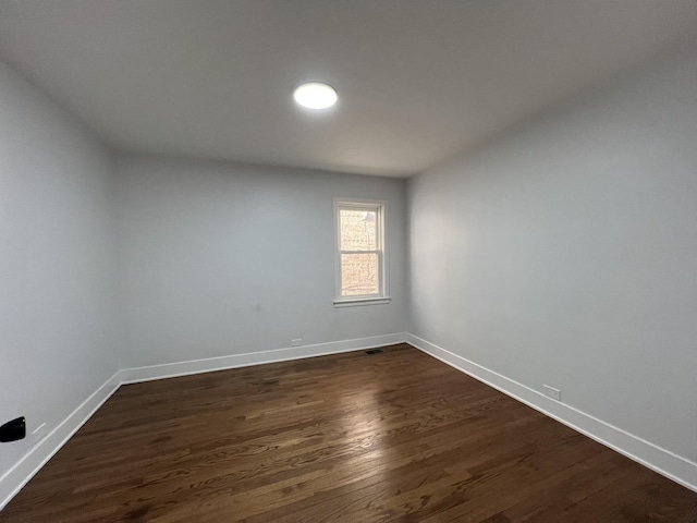 unfurnished room featuring dark wood finished floors, visible vents, and baseboards