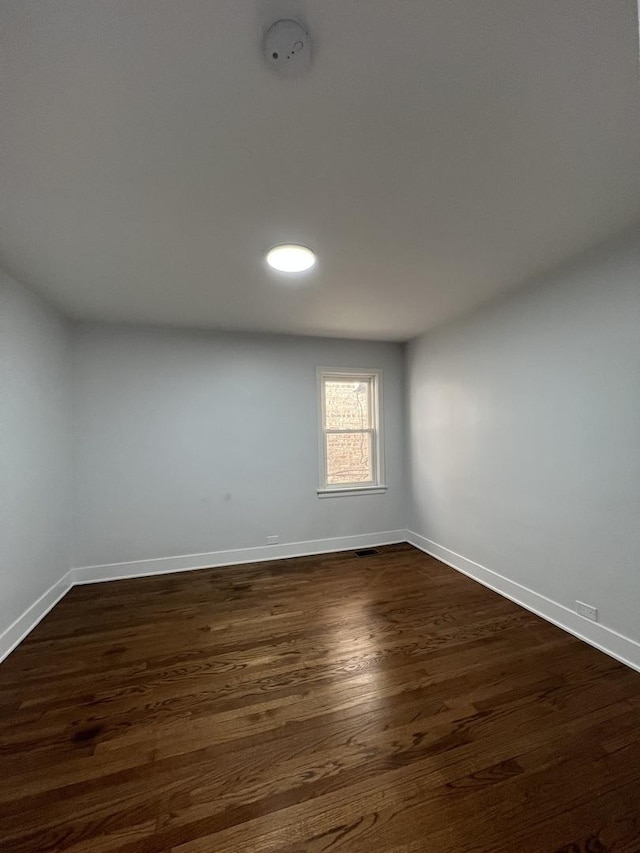 empty room featuring dark wood-type flooring, visible vents, and baseboards