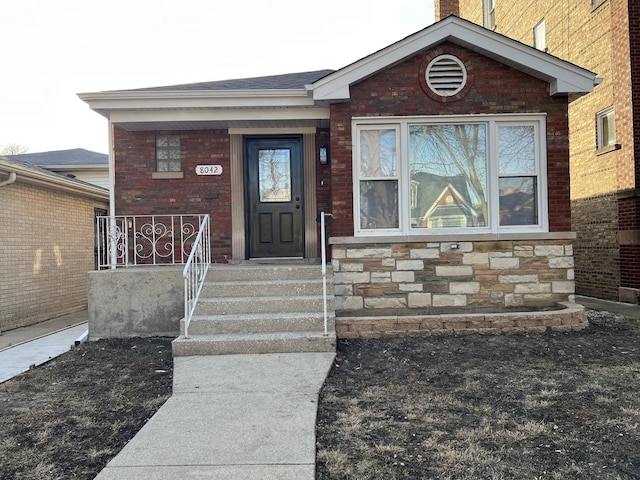 view of exterior entry with brick siding, stone siding, and covered porch